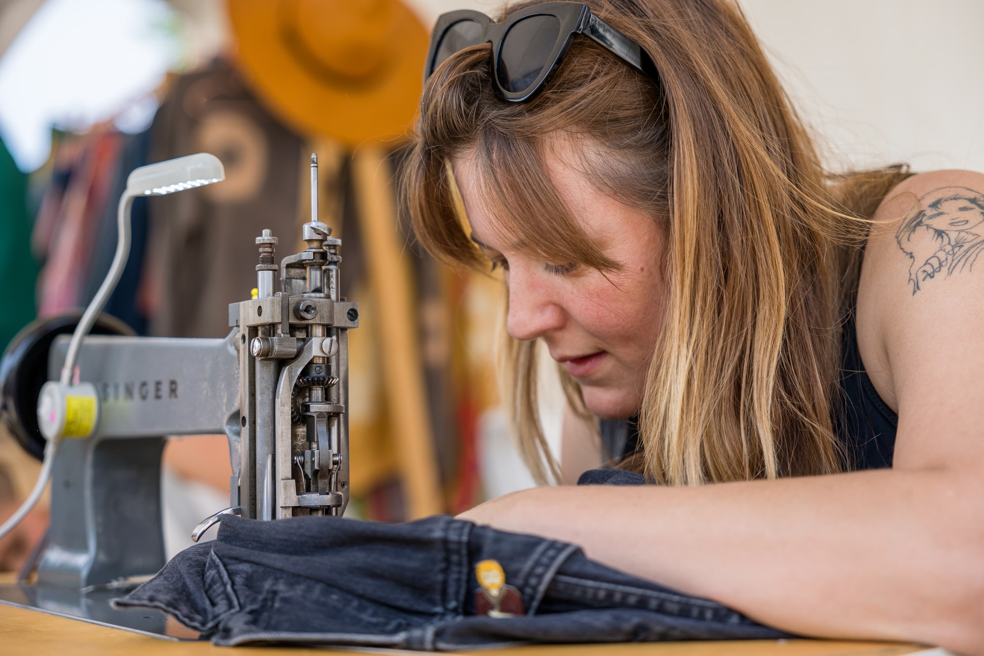 A woman uses a sewing machine to stitch on denim.
